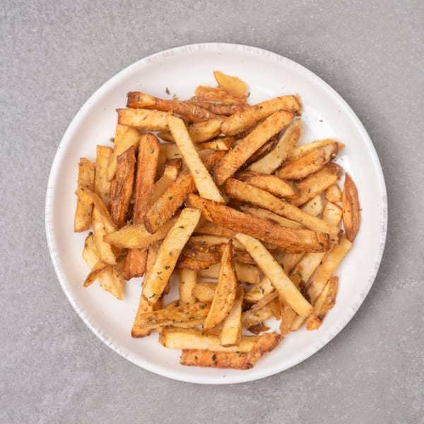 A white plate filled with golden-brown, seasoned french fries on a gray background.