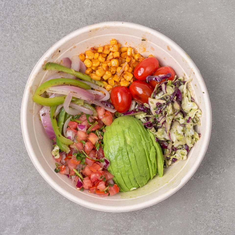 Overhead view of a colorful bowl with corn, tomatoes, avocado, pico de gallo, and cabbage slaw.