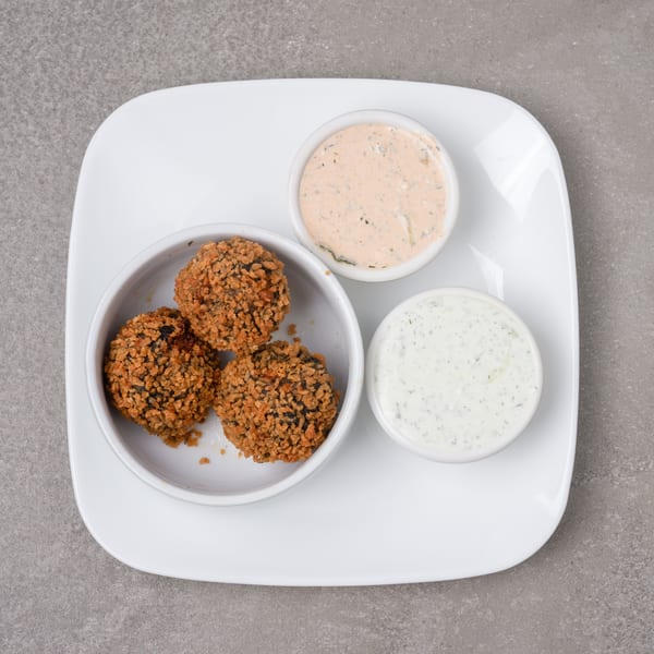Three crispy fried falafel balls in a white bowl, with two dipping sauces on a white plate.