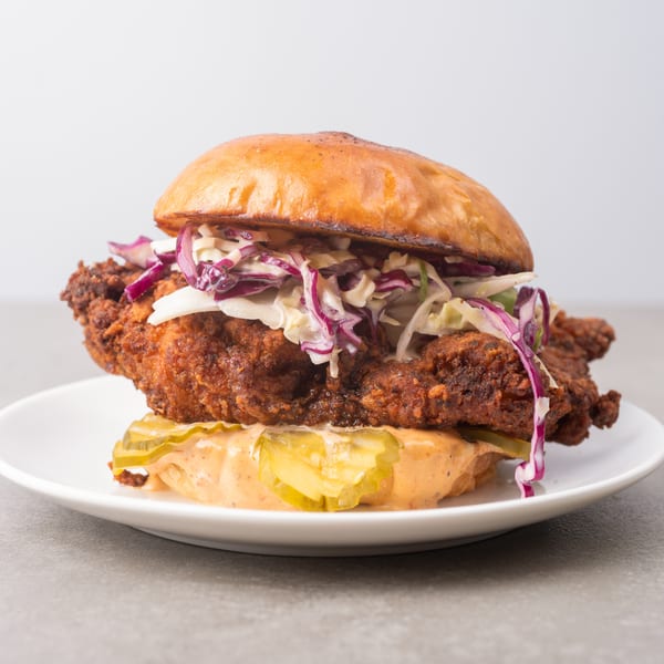 Crispy fried chicken sandwich with coleslaw, pickles, and sauce on a brioche bun.