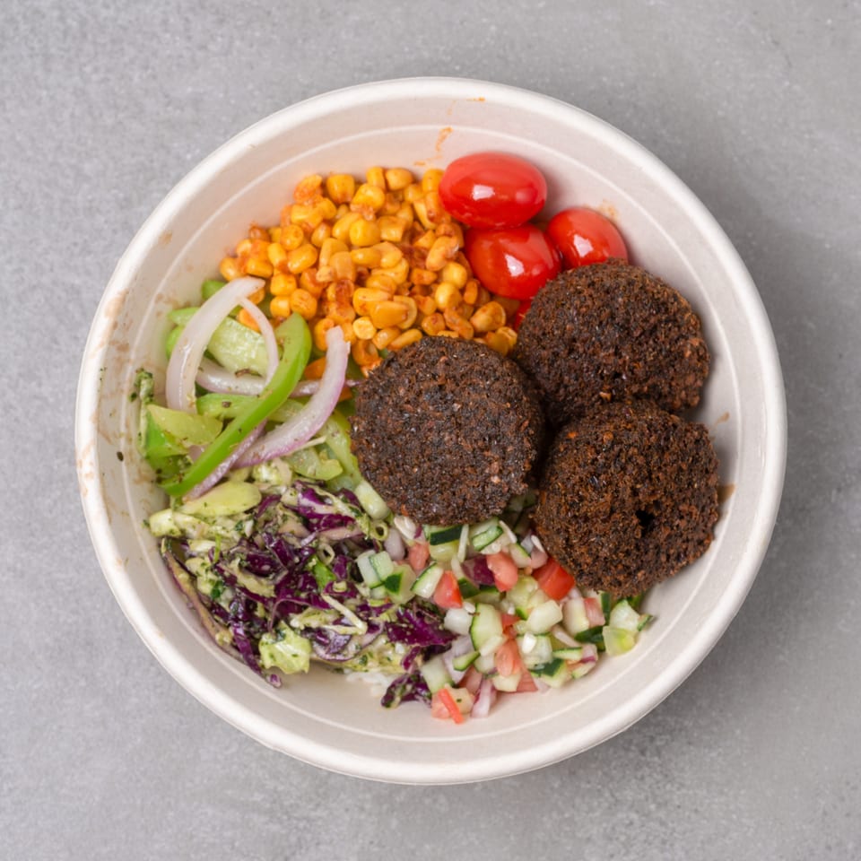 Falafel bowl with corn, cherry tomatoes, red cabbage slaw, and cucumber salad.